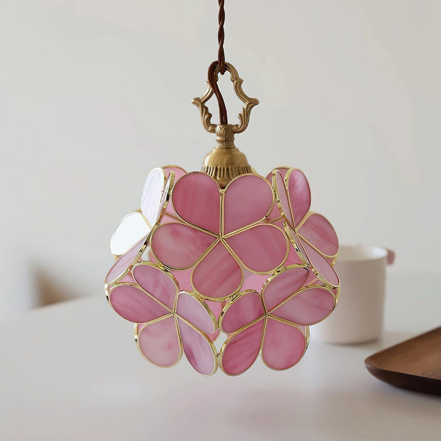 Brass and pink stained glass floral pendant lamp hanging above white cup and wooden tray