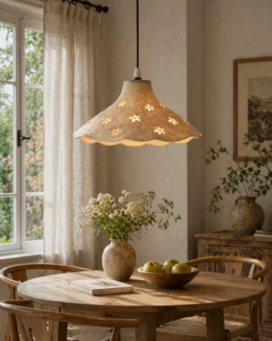 Ivory floral pendant light suspended over farmhouse dining table, warm rustic cottage aesthetic with natural wood furniture, overhead lighting perspective