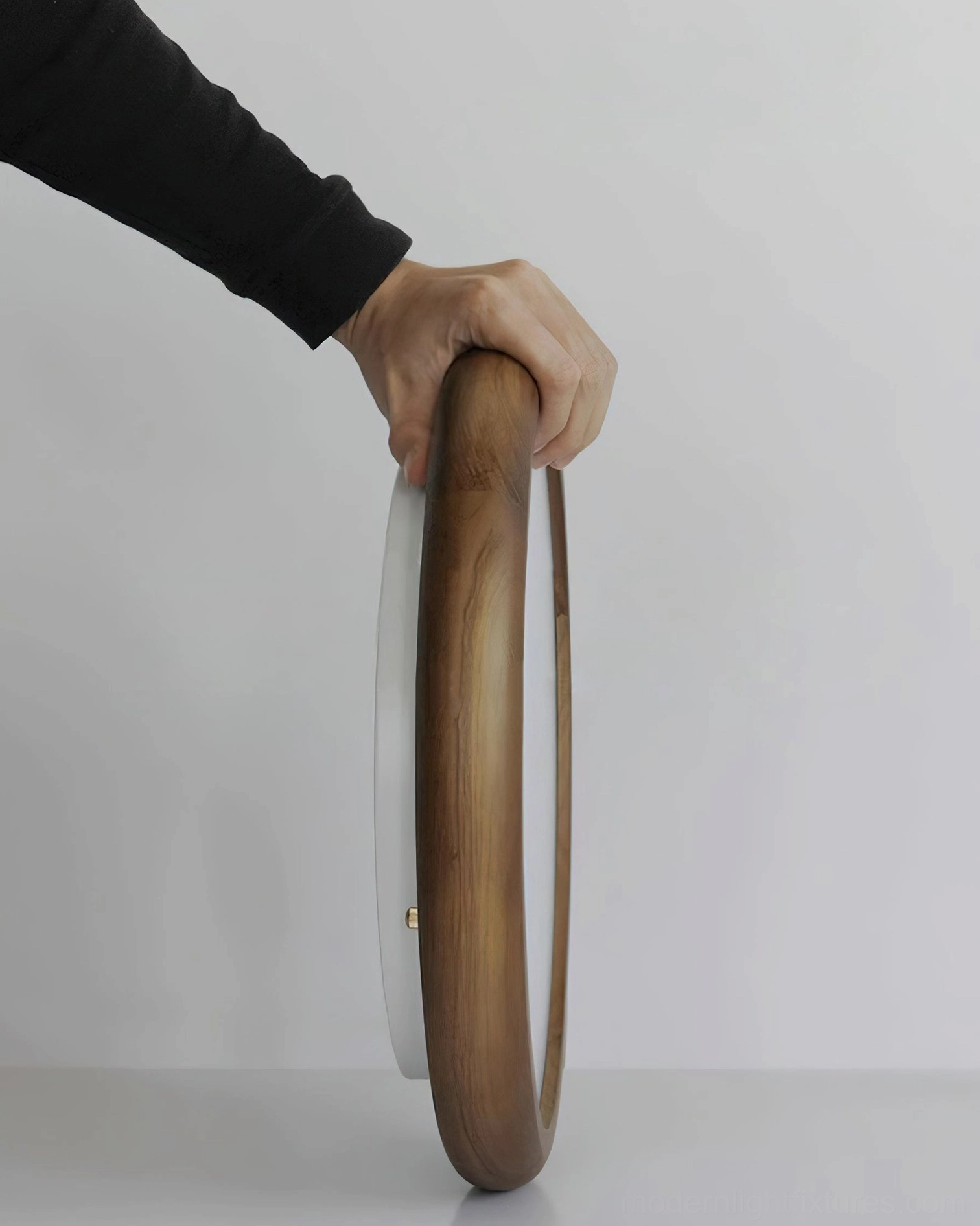 Natura ceiling lamp showing slim profile and natural wood ring frame held at angle, studio lighting detail
