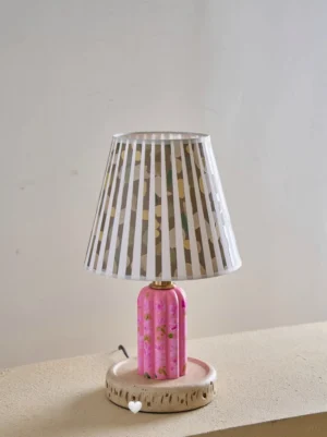 Modern floral table lamp three-quarter angle showing textured ceramic base with hand-painted botanical motif and tapered pleated lampshade