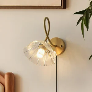 Floral wall lamp mounted in home interior with green plant accent, three-quarter perspective of ruffled glass shade