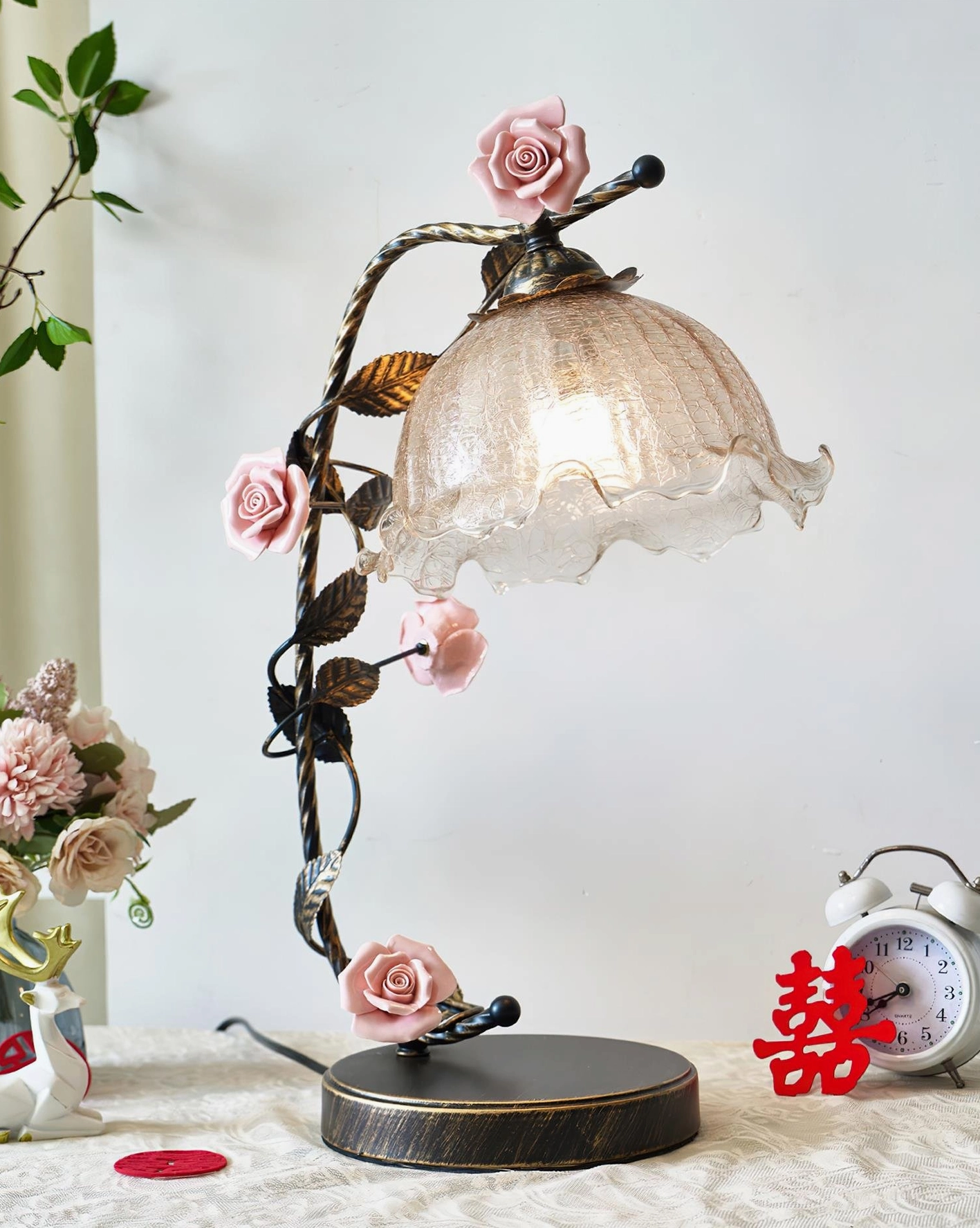 Florielle rose table lamp with black bronze vine frame and ruffled glass shade, left side angle view with floral arrangement