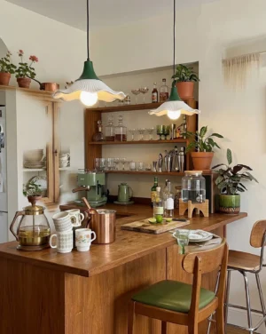 Pair of fluted pendant lights in vintage kitchen with green and burgundy metal tops above wooden bar with houseplants and tableware