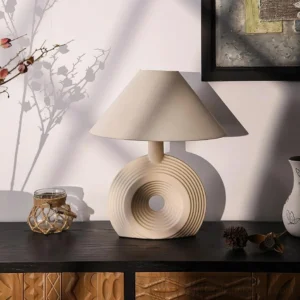 Freya modern ceramic table lamp illuminated on wooden sideboard with warm golden glow and concentric ripple base
