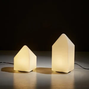 Pair of contemporary gabled-top ceramic table lamps glowing with warm ambient light in minimalist interior setting