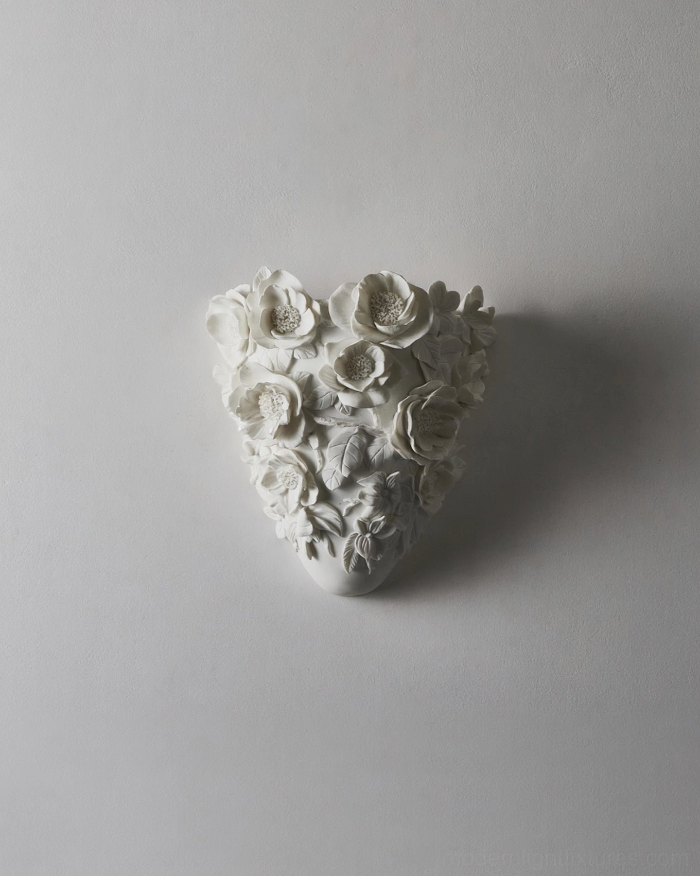 Matte white sculptural gardenia wall sconce on neutral gray wall, artistic shadow casting