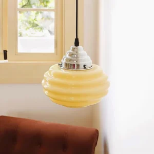 Beige gelato pendant light installed in cozy living room with brown tufted sofa, three-quarter side view showing suspension cord and polished chrome mount