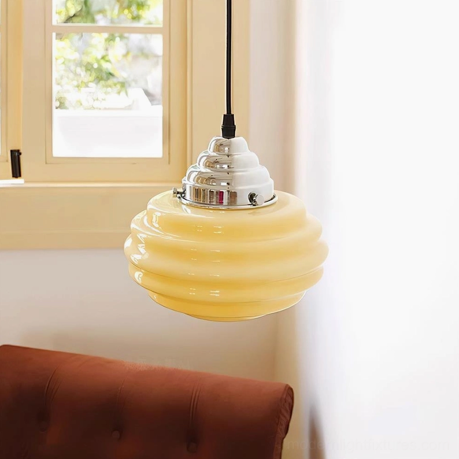 Beige gelato pendant light installed in cozy living room with brown tufted sofa, three-quarter side view showing suspension cord and polished chrome mount