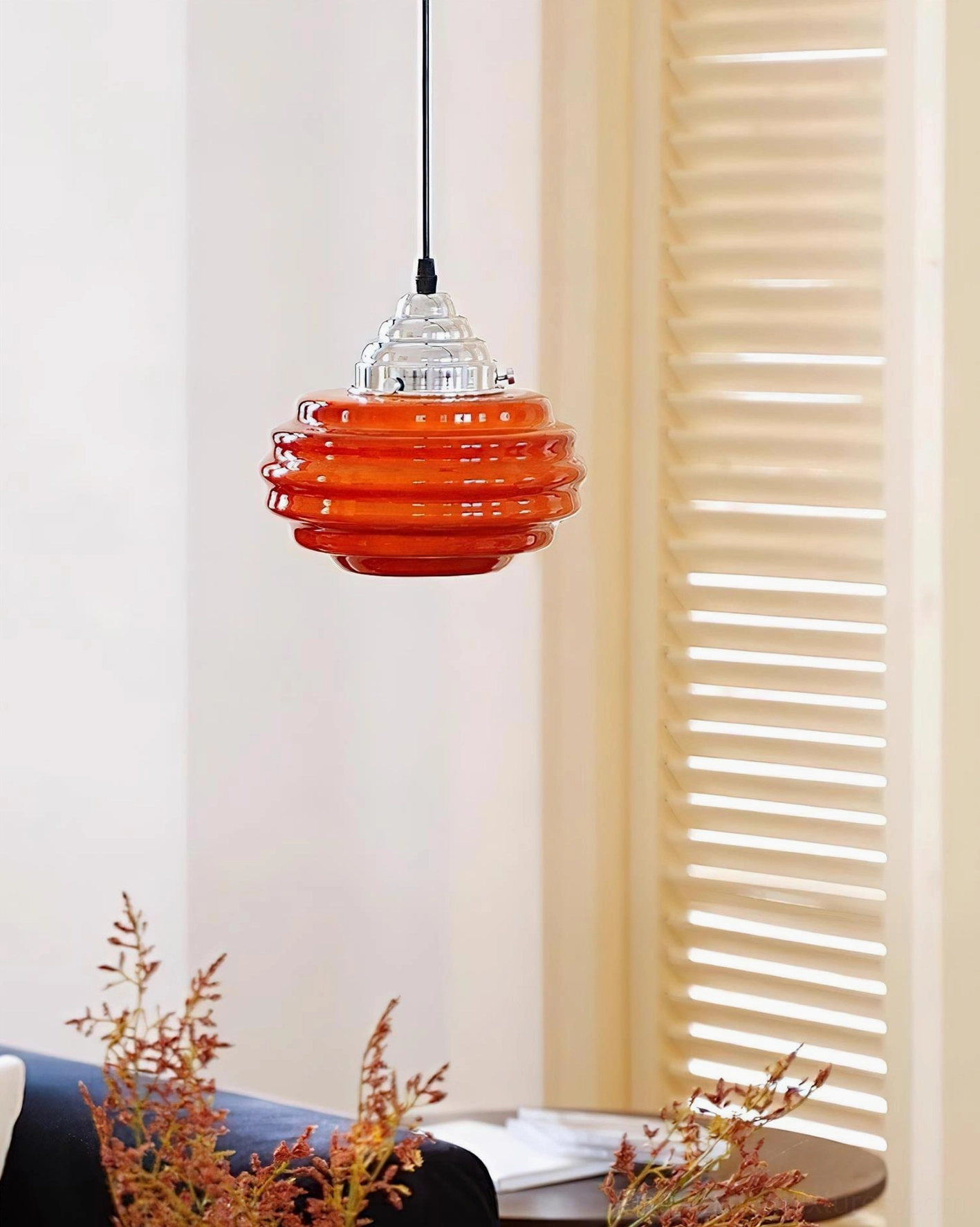 Bright orange gelato pendant light three-quarter side view in living room with louvered shutters and decorative plant styling