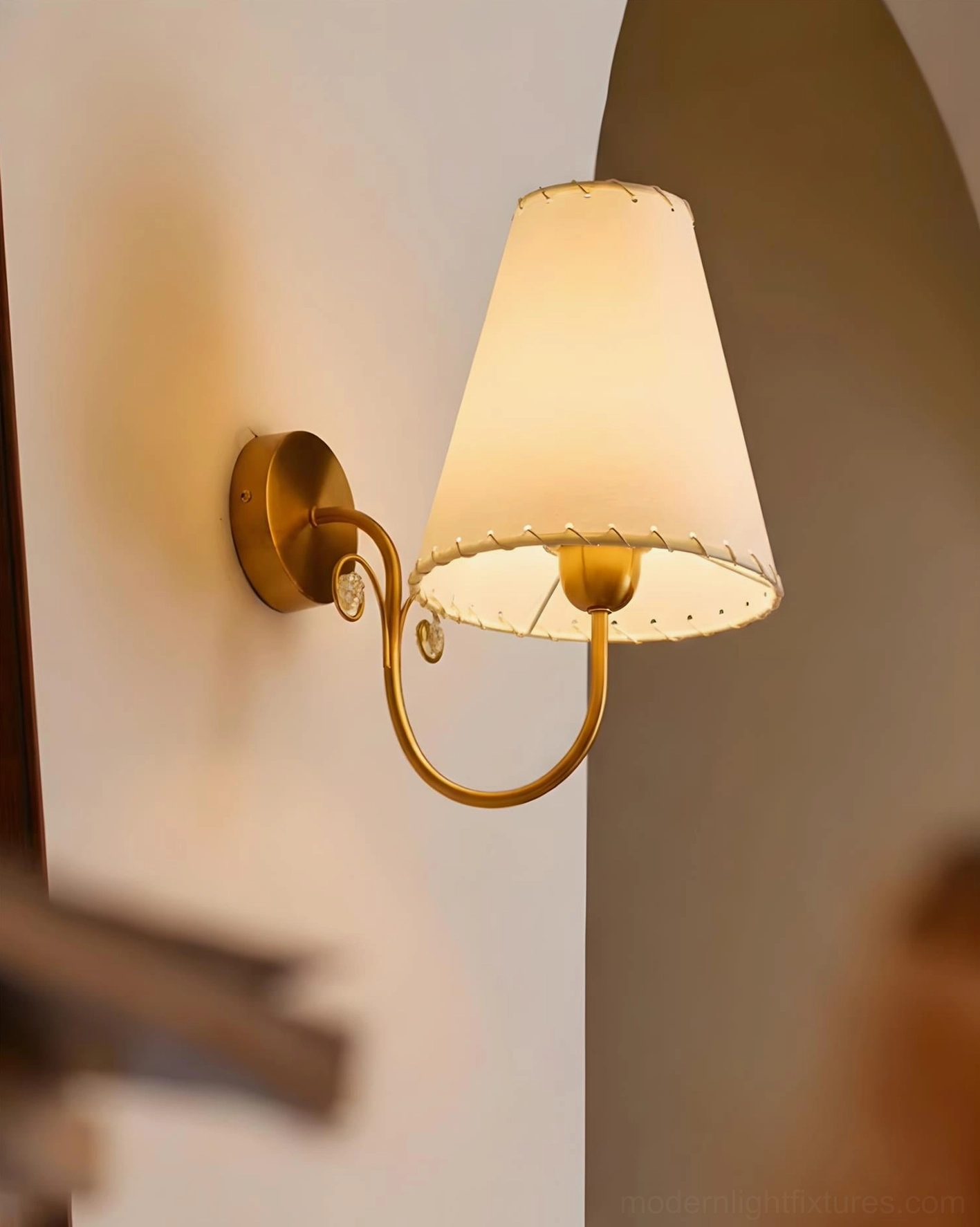 Gentle Bend fabric wall sconce lit in arched wall corner residential interior with warm brass glow