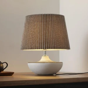 Modern ceramic table lamp Ghassan illuminated on wooden side table with warm ambient light, three-quarter view