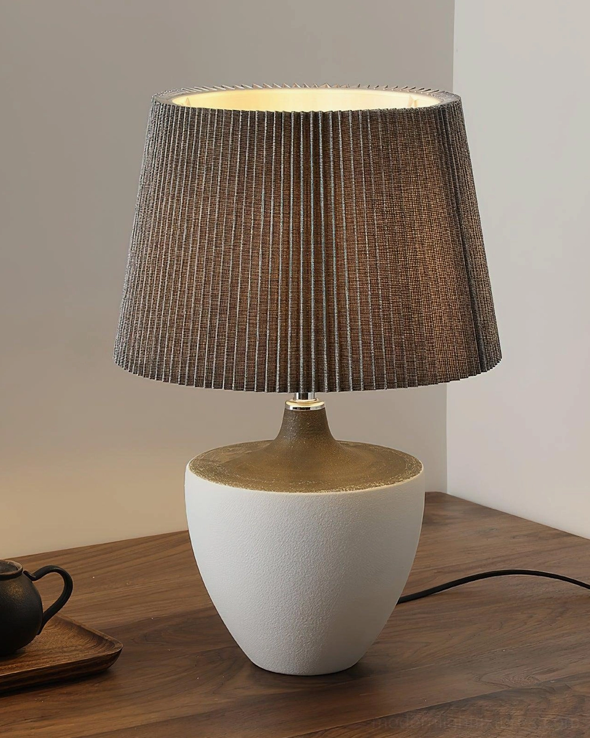 Ghassan ceramic urn-shaped table lamp with white matte base and brown pleated fabric shade, wooden surface styling