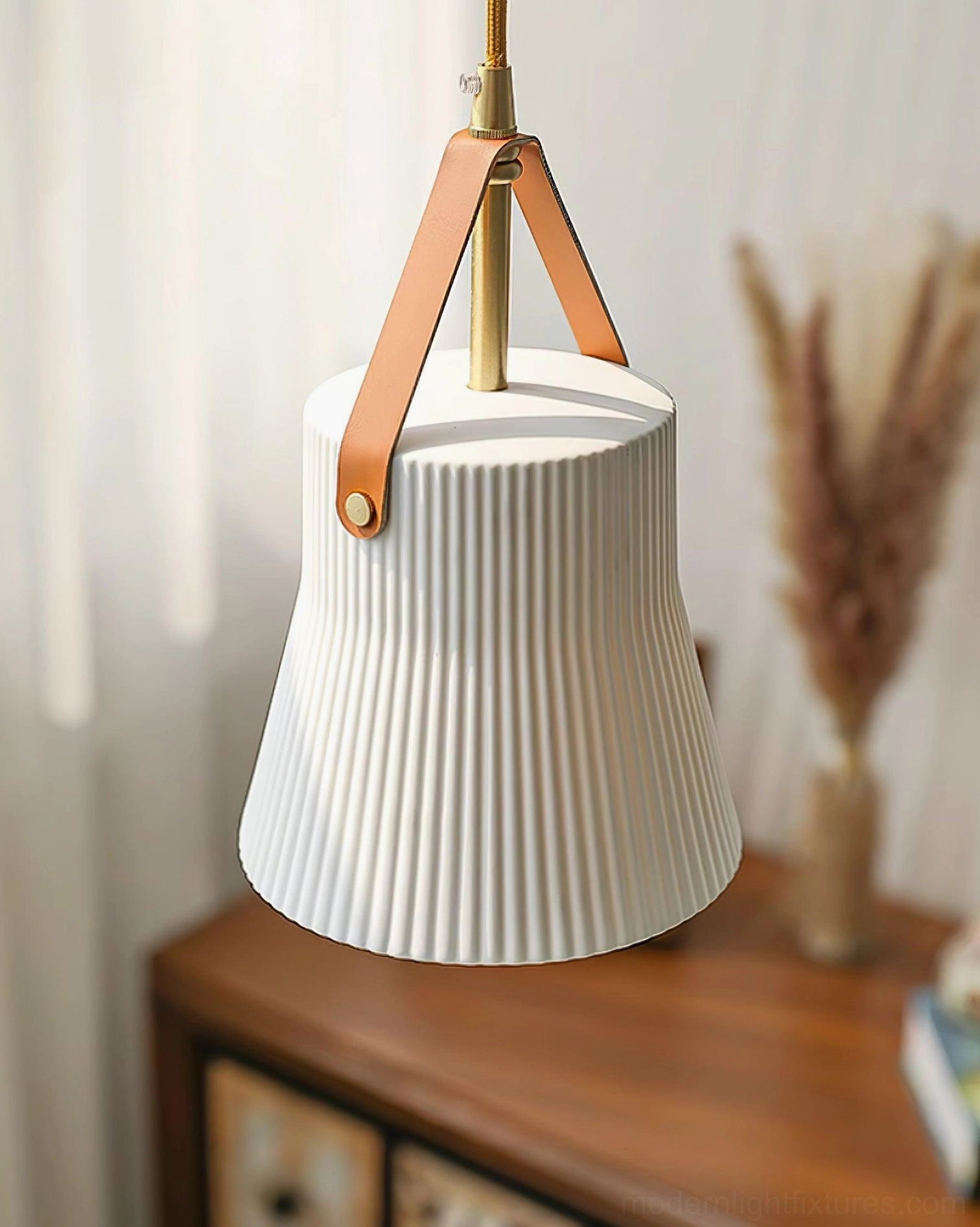 Wide flared ceramic ridged pendant lamp overhead view with tan leather strap and brass fixtures above wooden dresser