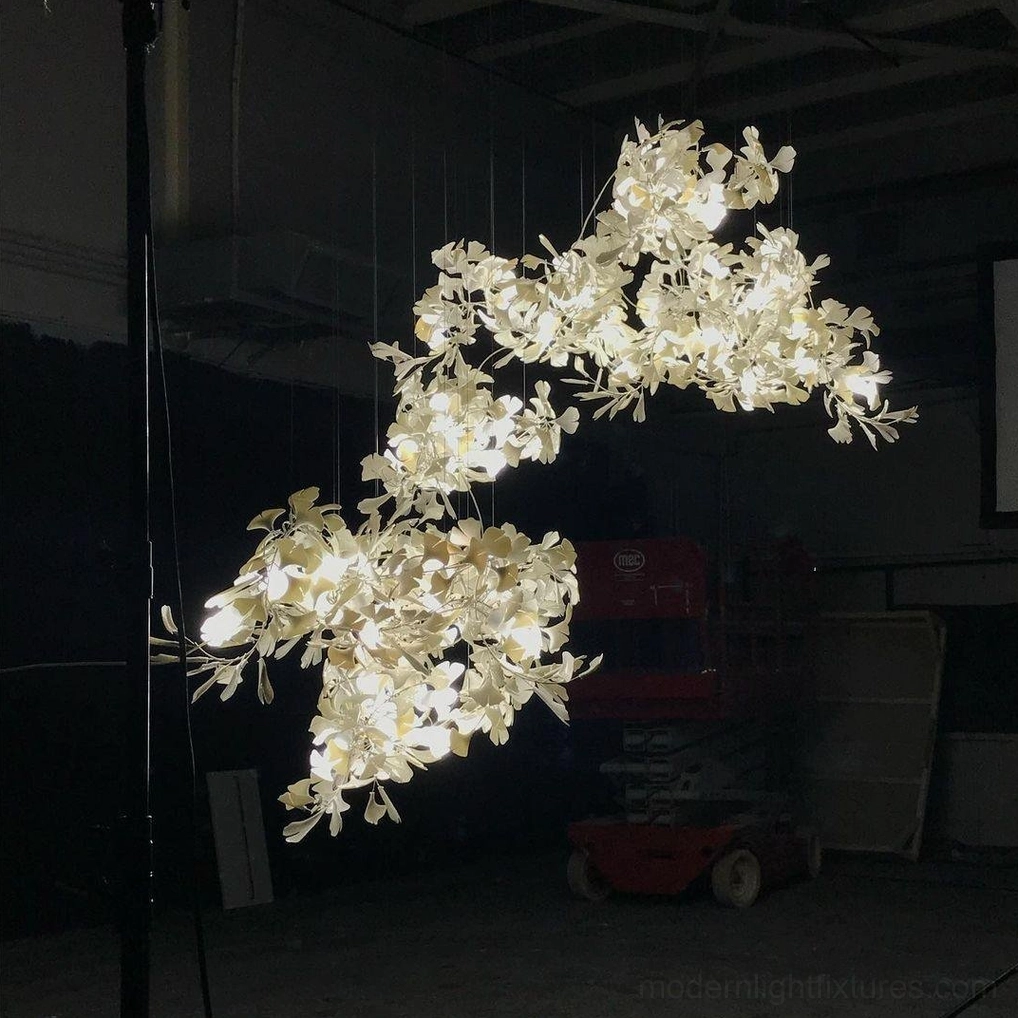 Side low-angle view of ginkgo chandelier in industrial warehouse showing warm lit leaf clusters and compact design