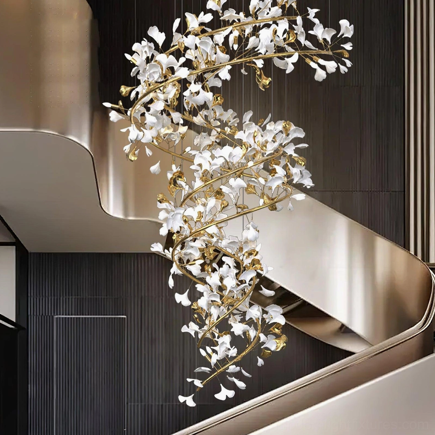 Spiral ginkgo leaf chandelier with gold metal branches and crystal leaves beside dark paneled modern staircase with metal handrail