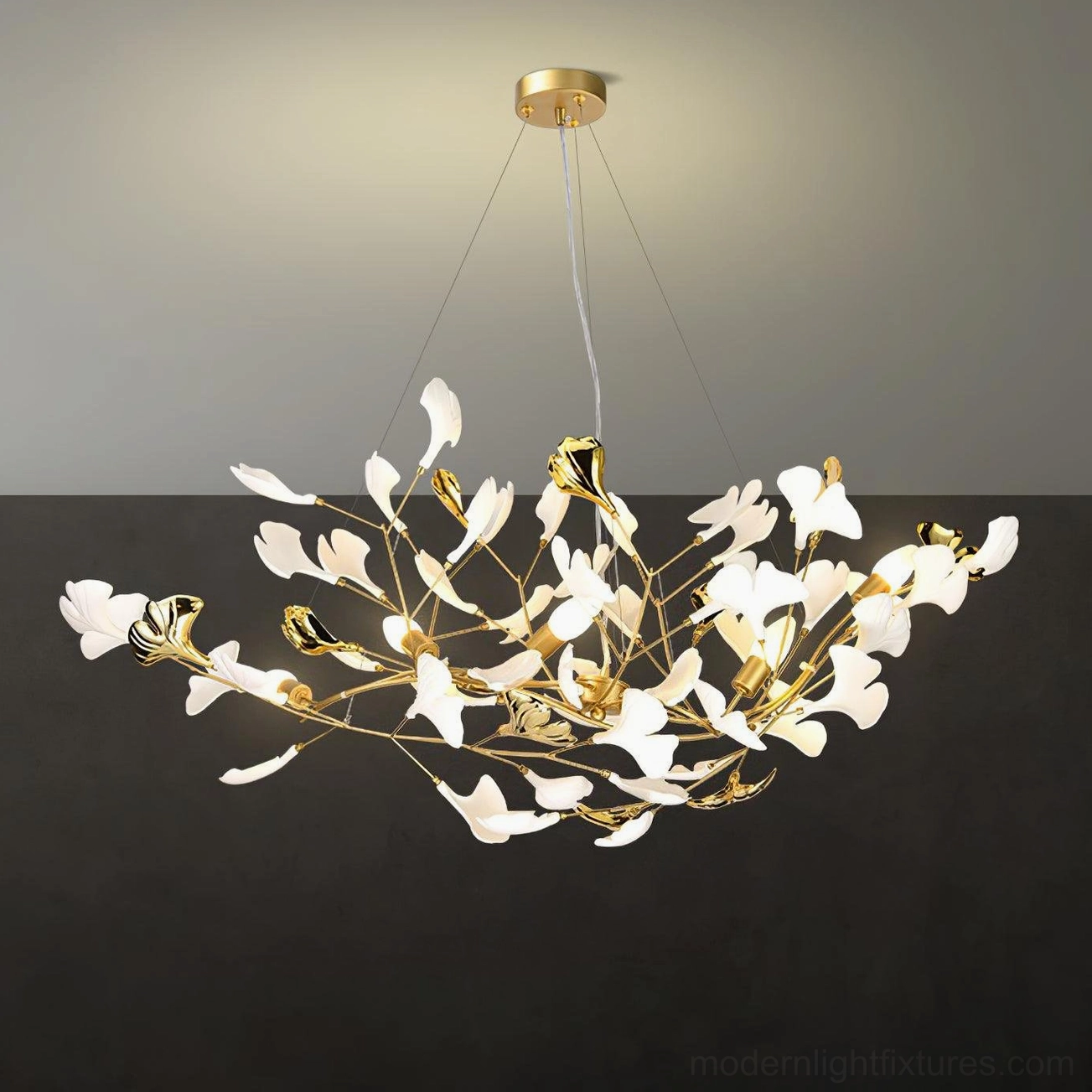 Close-up detail of ginkgo leaf ceramic chandelier - gold metal frame and white ceramic leaves against dark accent wall