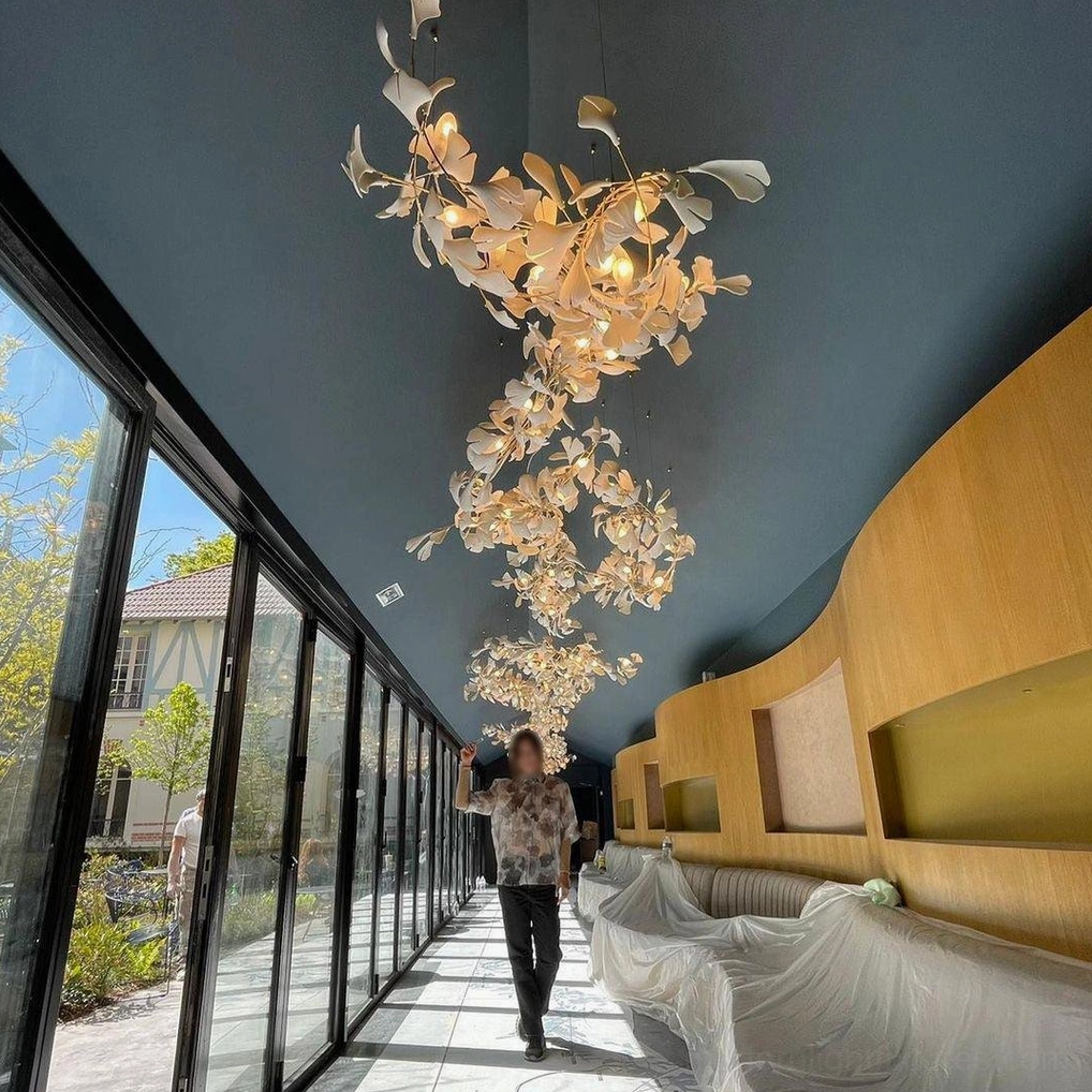 Multiple cascading ginkgo leaf chandeliers installed in upscale hotel retail corridor with warm gold tones creating grand artistic pendant light row display