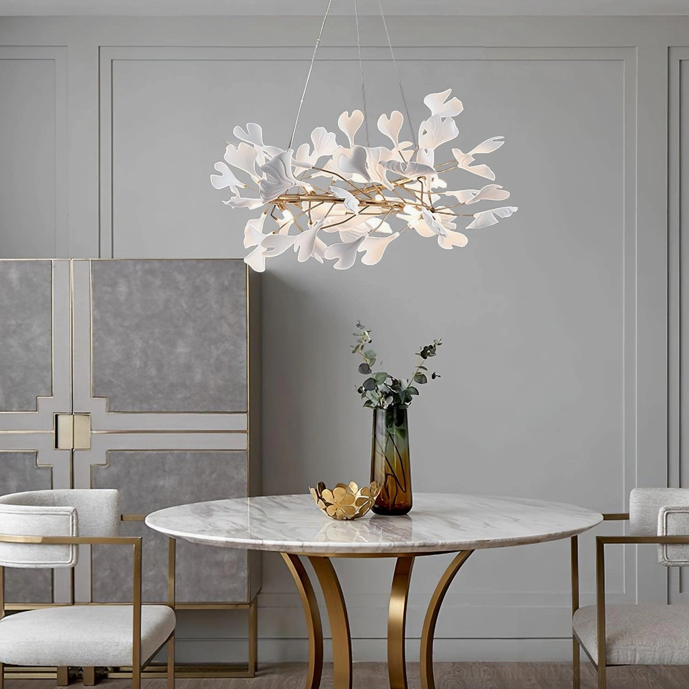Modern ginkgo leaf chandelier above marble round dining table with gold metal structure