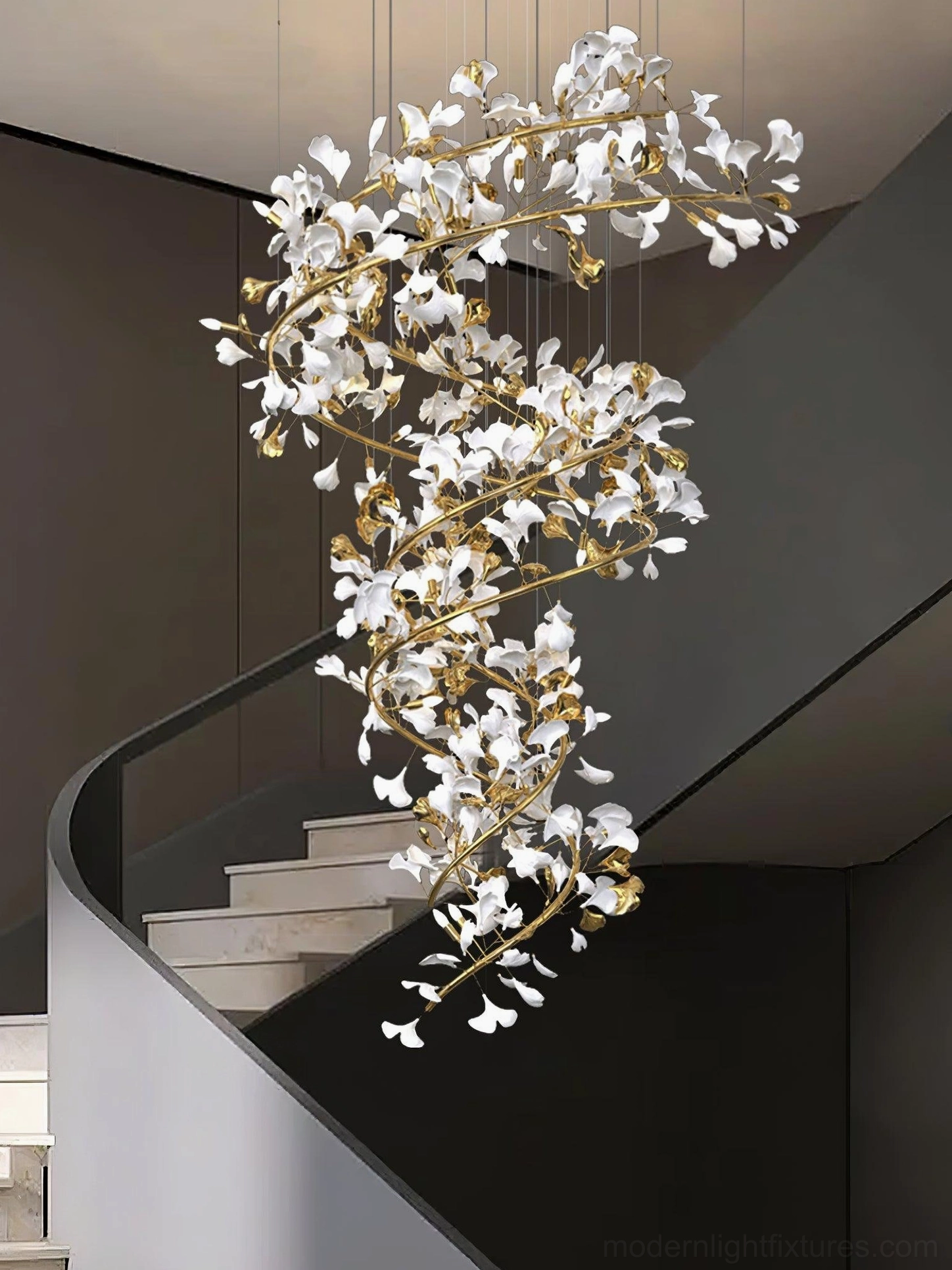 Side view of ginkgo leaf chandelier with gold frame and crystal leaf elements in modern villa spiral staircase setting