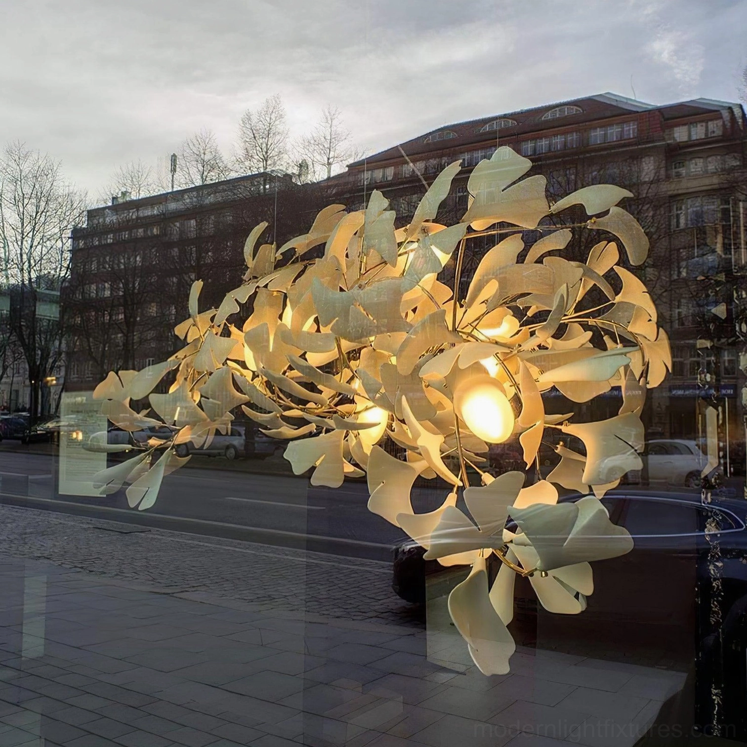 Ginkgo leaf chandelier outdoor street view with illuminated warm yellow bulbs, large-scale sculptural leaf structure, urban sidewalk display