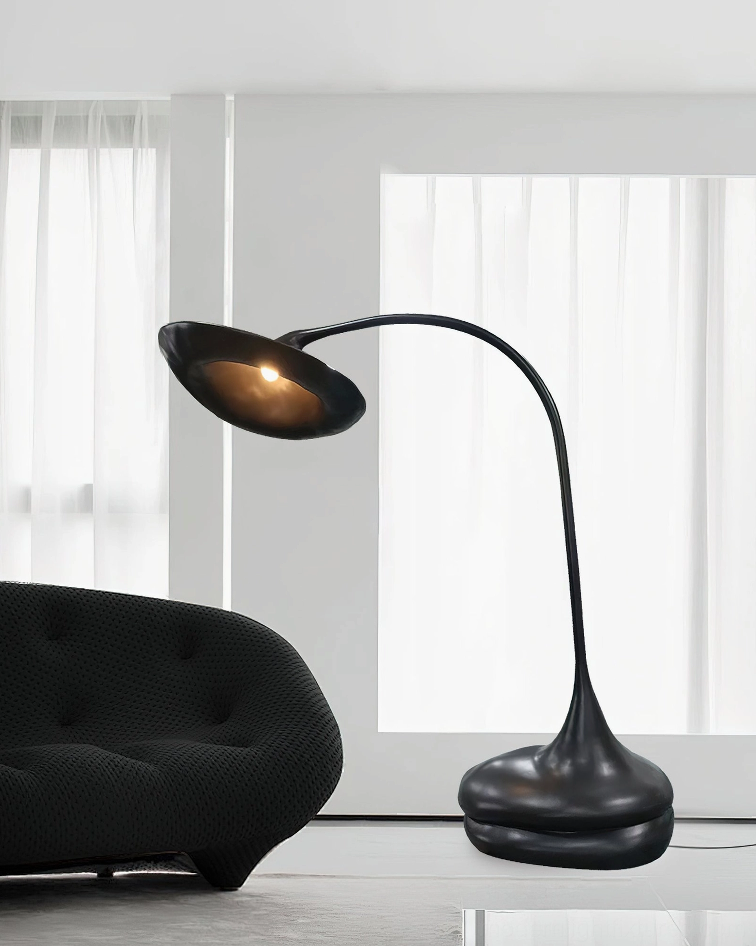 Black organic floor lamp beside curved tufted sofa in bright minimalist interior with sheer curtains