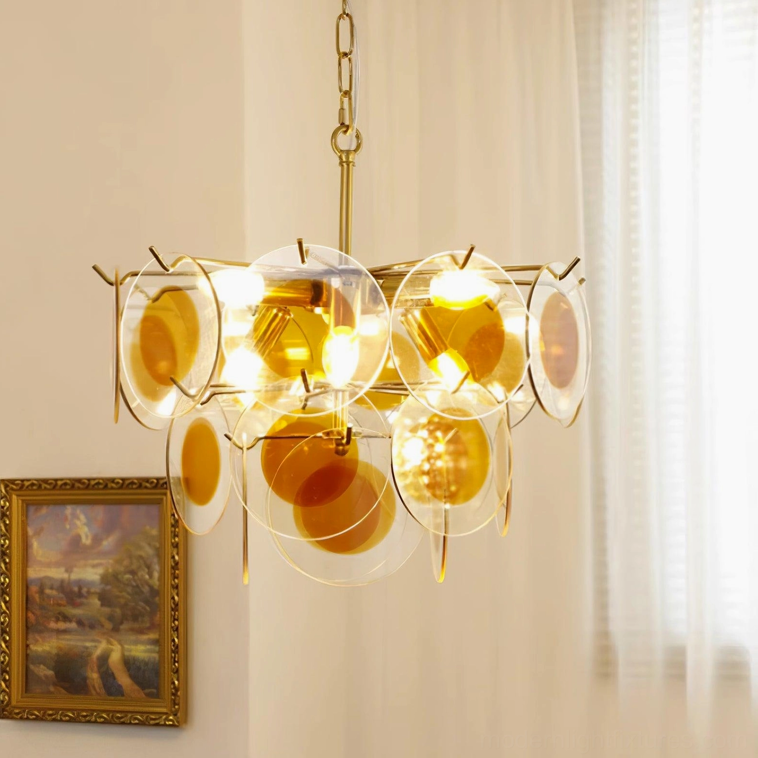 Glass disc pendant chandelier amber brass gold illuminated in residential interior with curtains and wall art