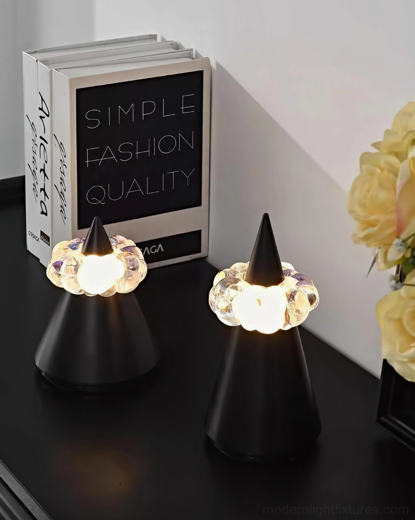 Matte black minimalist cone lamp with illuminated crystal diffuser paired on black side table with books and floral decor, modern home accent