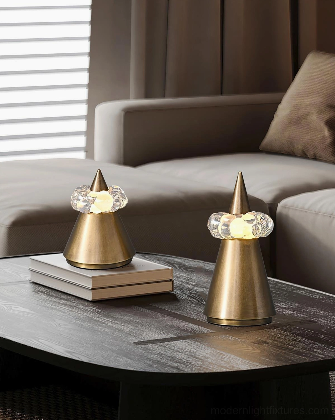 Two brushed bronze sculptural table lamps on contemporary living room coffee table with books and modern sofa background