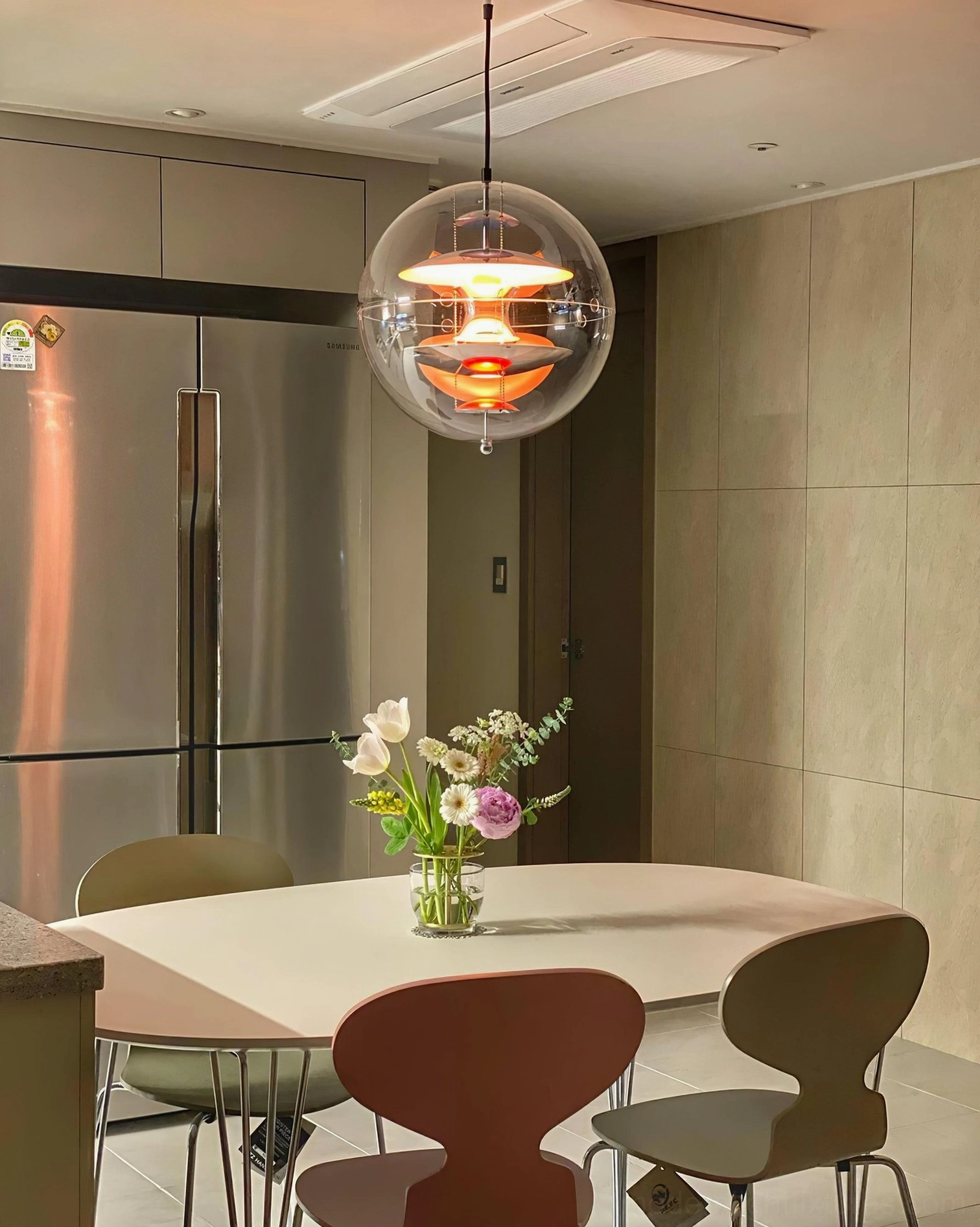 Illuminated globe pendant light in kitchen-dining hybrid space with stainless steel refrigerator backdrop and warm gold-red interior structure
