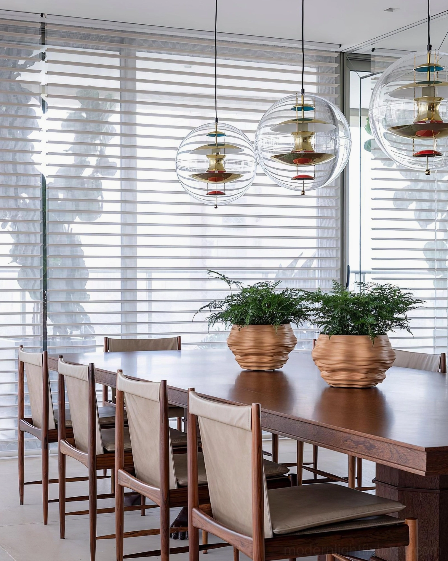 Three globe pendant lights hanging over long dining table in bright modern dining room with window blinds and minimalist decor