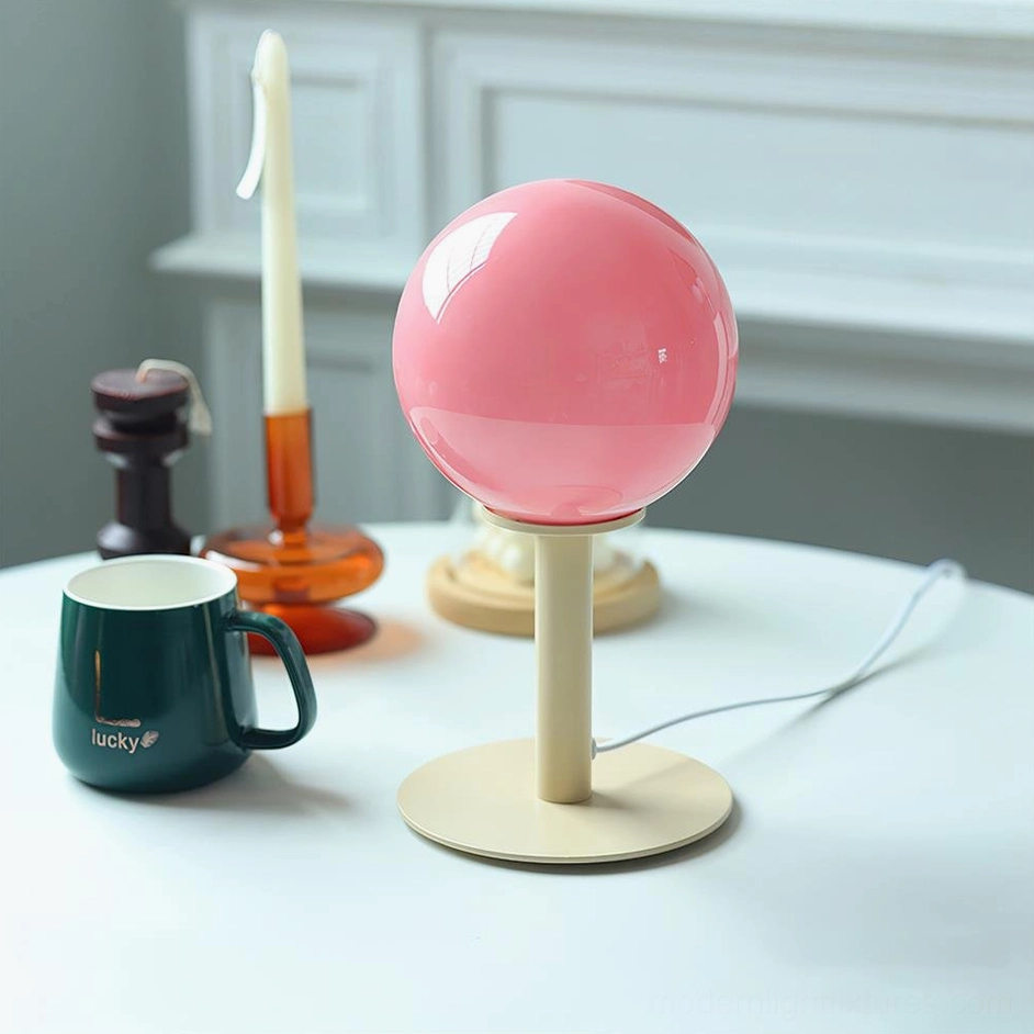 Modern globe table lamp with beige metal base and pink glass shade in contemporary dining setting