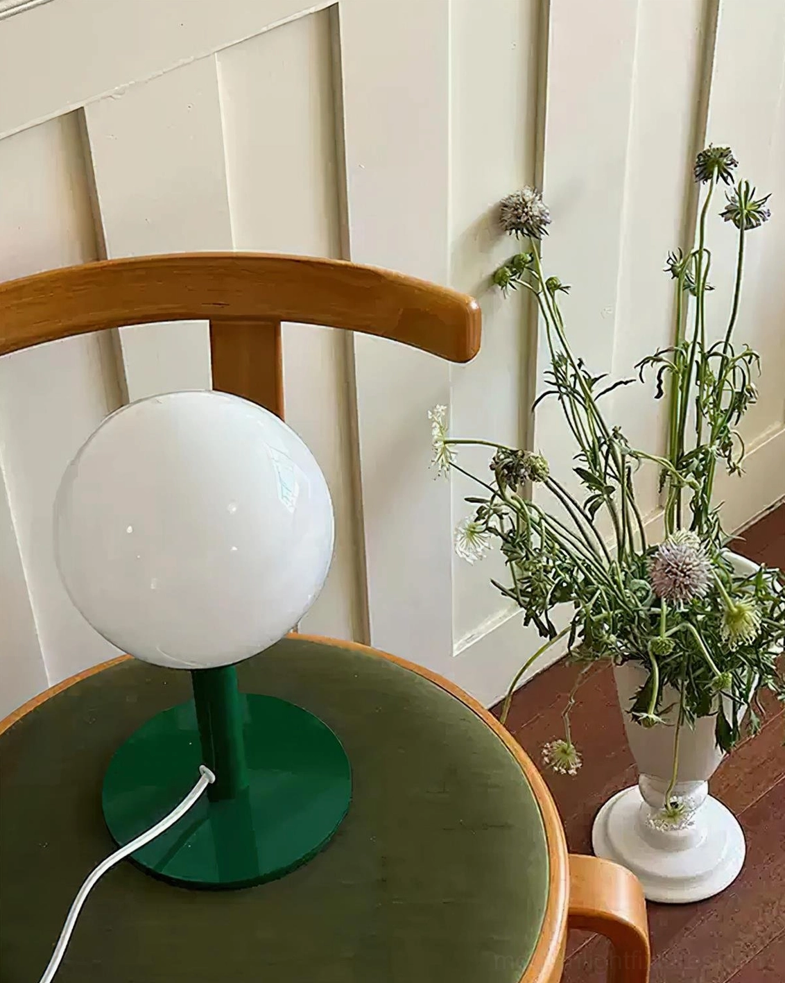 Minimalist globe table lamp with dark green base and white shade in cozy dining nook with floral décor