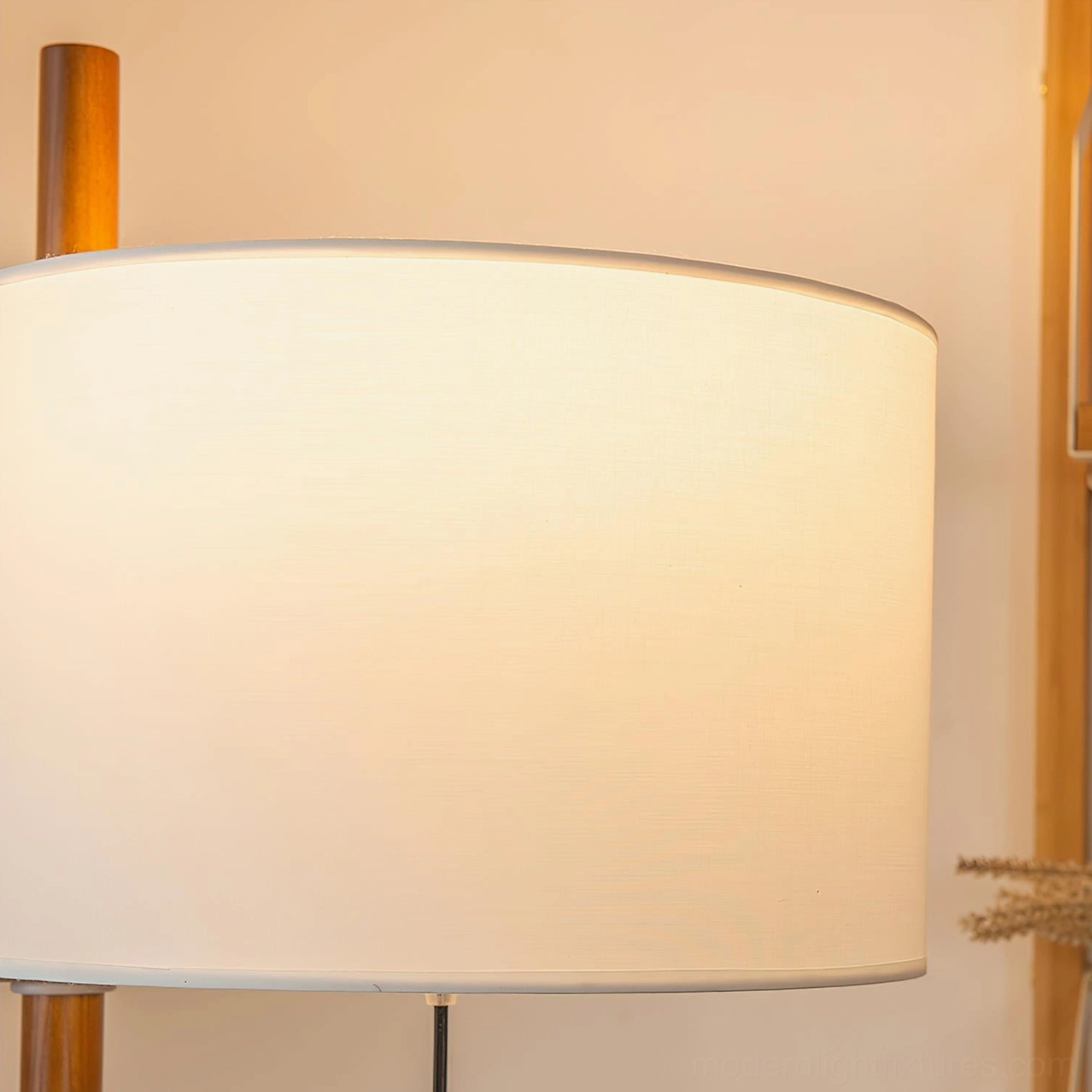 Illuminated lampshade close-up showing soft warm fabric glow with golden finial detail on wooden pole