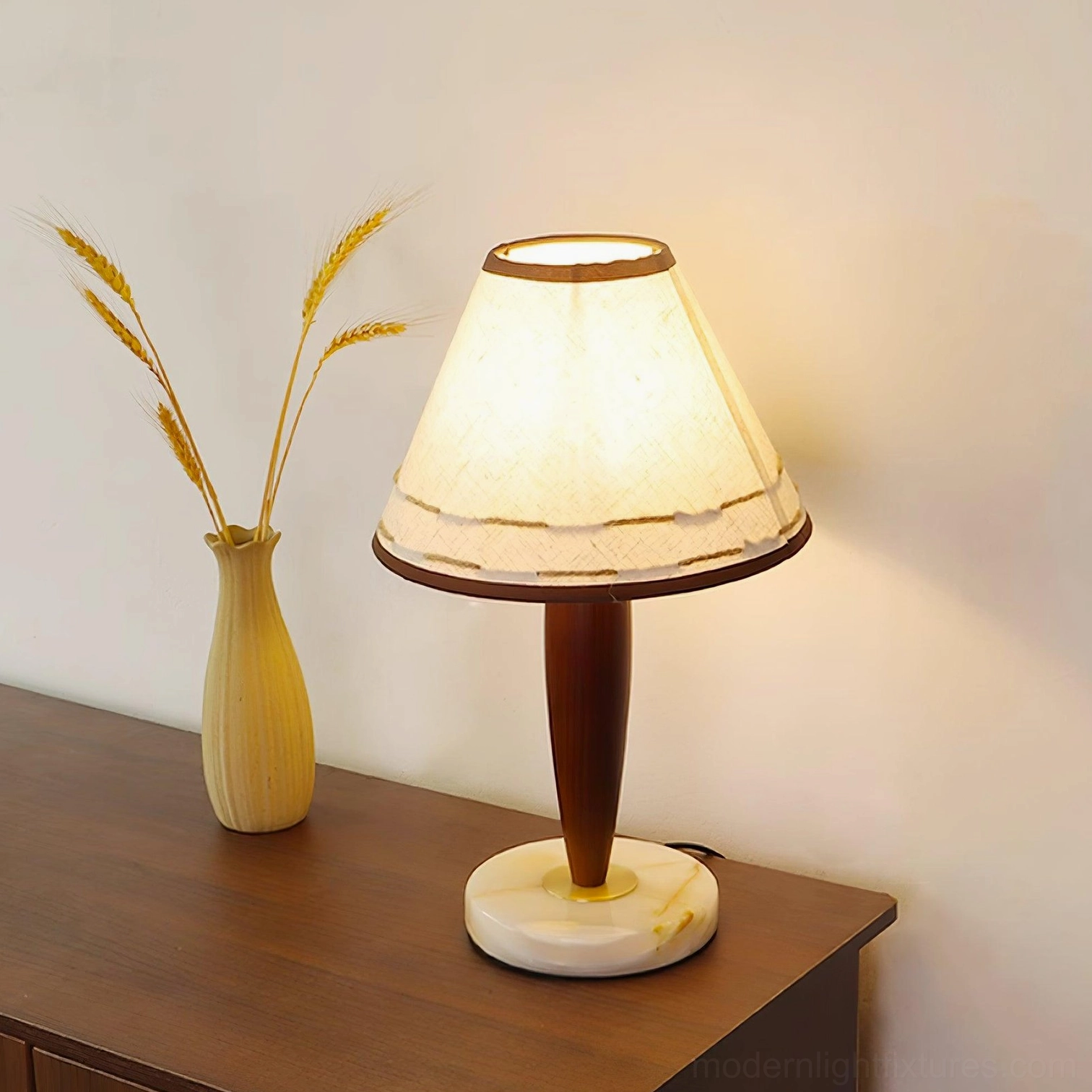 Illuminated terracotta table lamp on wooden table with yellow wheat vase - warm ambient lighting