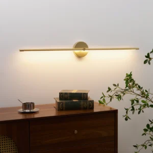 Brushed gold linear wall sconce mounted above wooden cabinet with warm ambient lighting and green plants