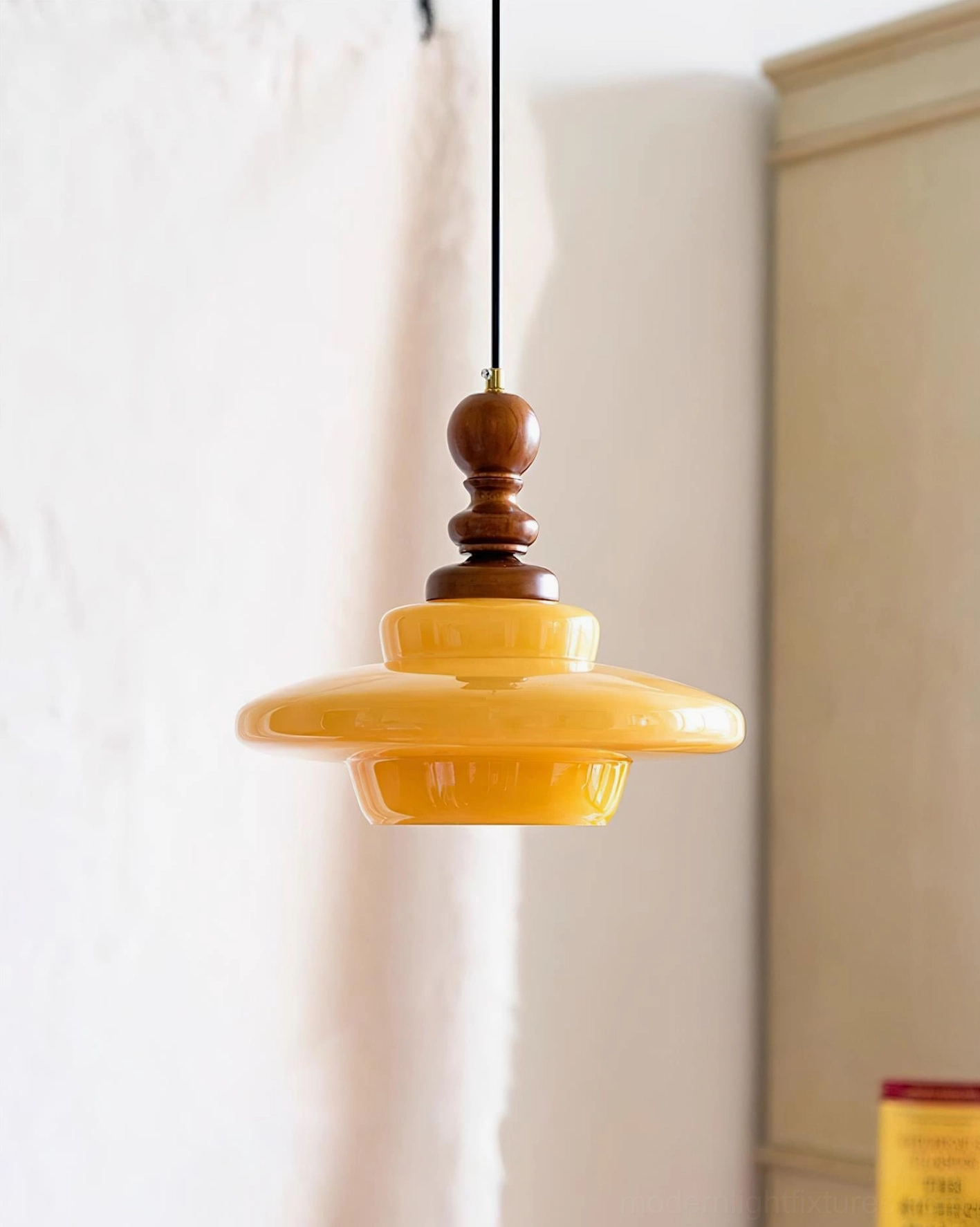 Mustard yellow pendant light fixture hanging indoors, showing warm glass shade with matching wooden hardware and cabinet background