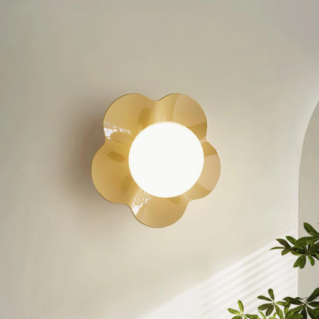 Golden yellow Fleur wall sconce close-up mounted on beige wall with green plant decor - illuminated frosted glass center