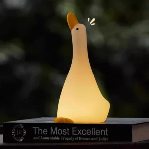 Illuminated goose night light glowing warm white 3000K LED on desk next to open book, demonstrating circadian-friendly ambient lighting for workspace and reading