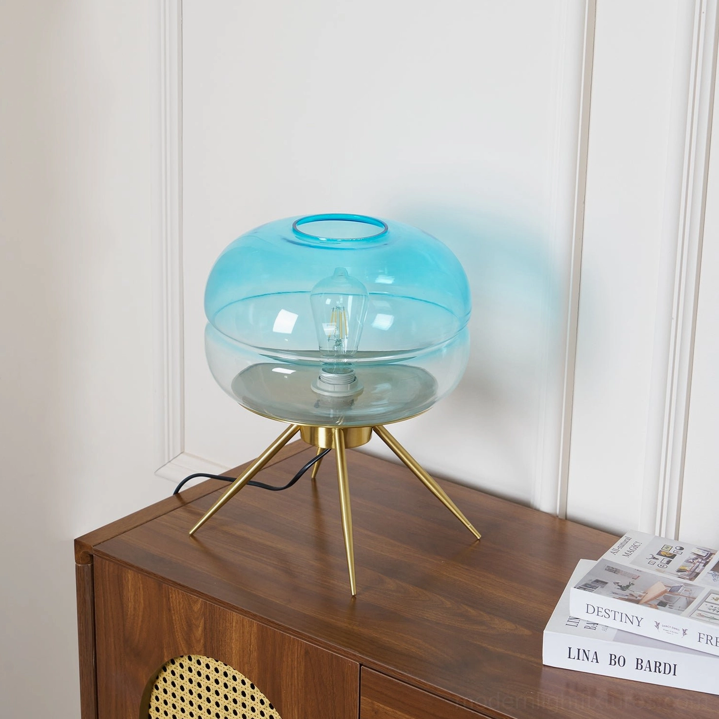 Unlit gradient blue tiered glass lamp base on dark wood cabinet with magazines styling
