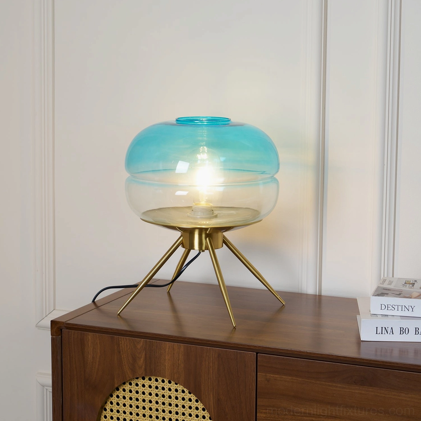 Cyan gradient glass tiered table lamp in three-quarter view on bookshelf with paneled white wall background