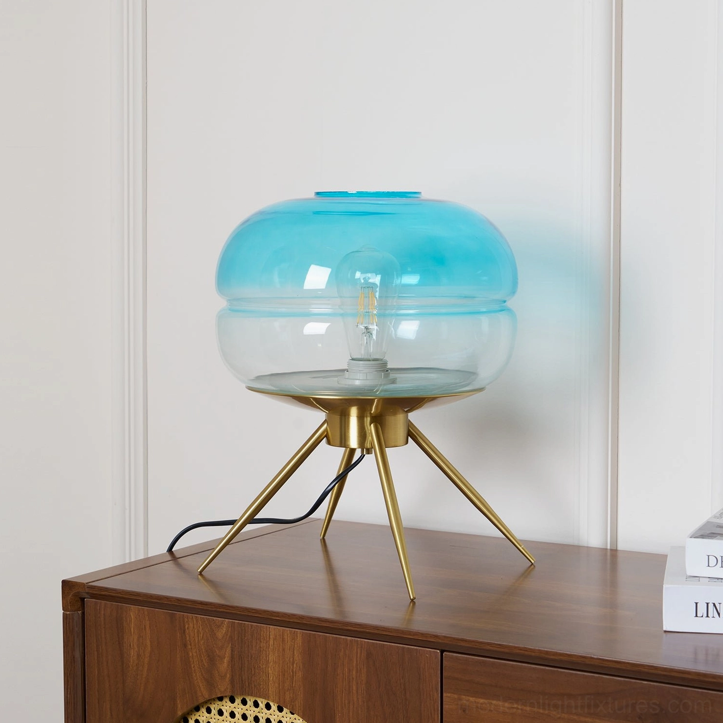 Gradient blue tiered glass table lamp illuminated on dark wood cabinet with stacked books in interior display