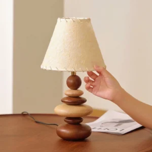 Close-up three-quarter view of Grainelle table lamp showing hand adjusting whipstitched edge detail on linen shade, demonstrating craftsmanship
