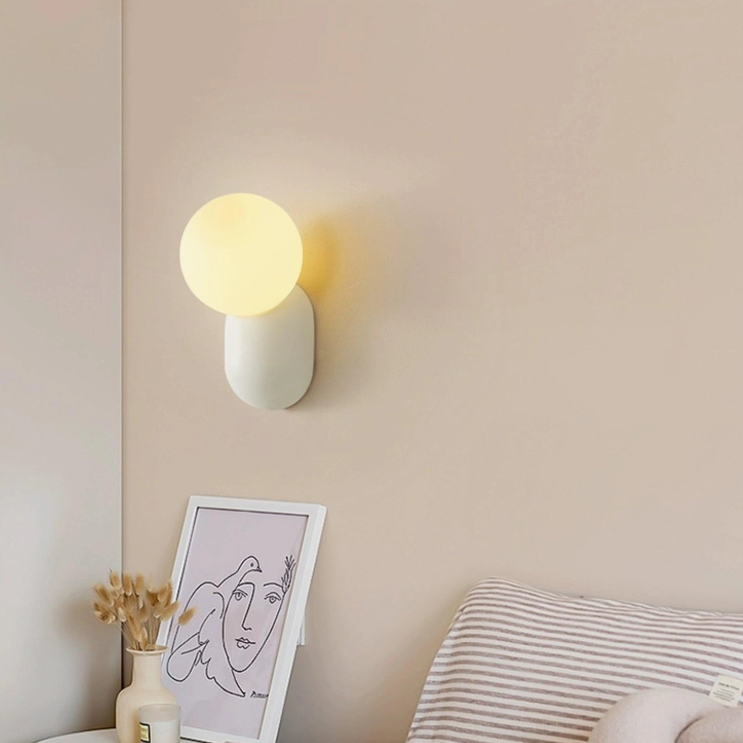 Single light gray spherical wall sconce installed beside bedroom bed emitting warm yellow light, side view