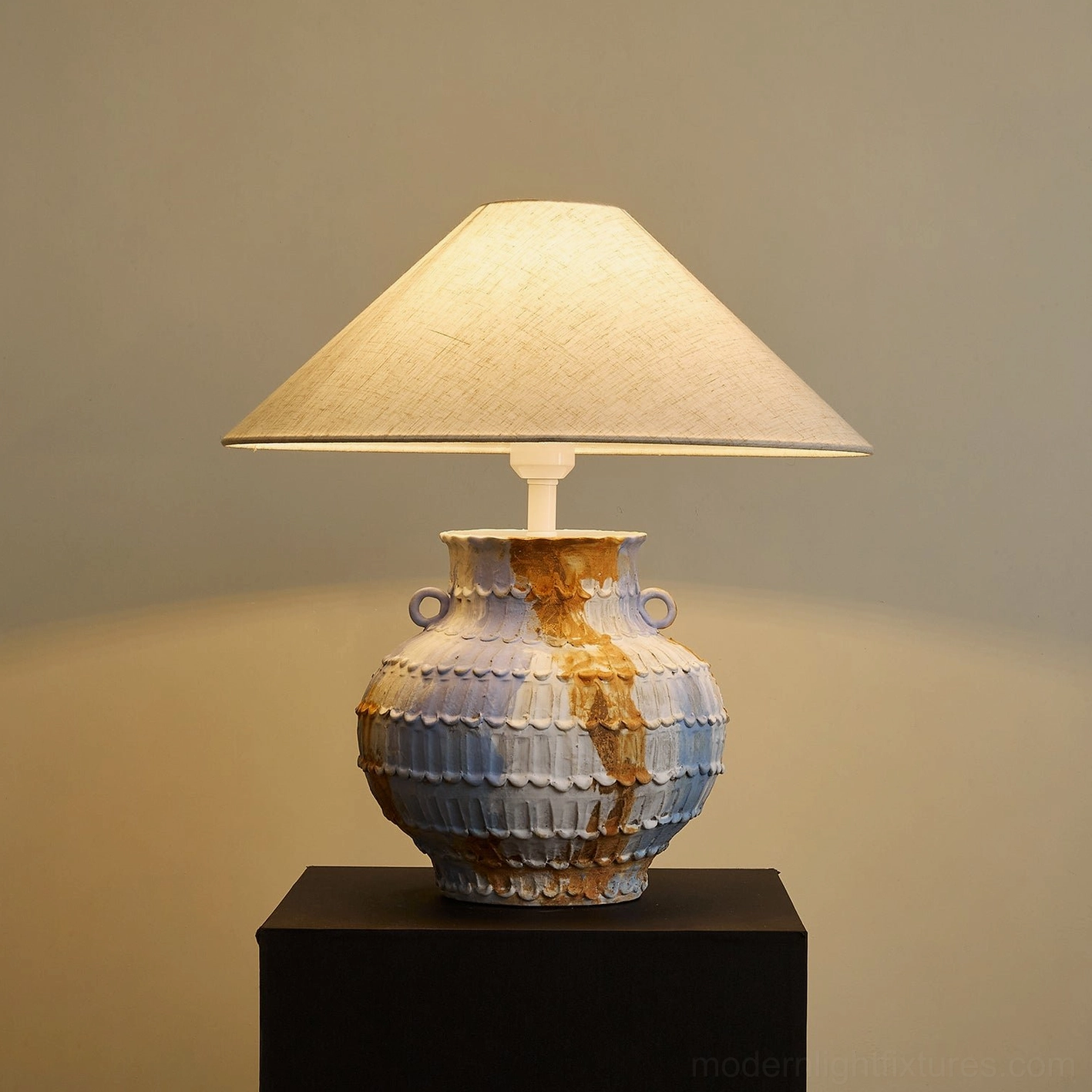 Grazie table lamp three-quarter lit view showing conical linen fabric shade and ribbed sculptural ceramic pot base with artistic blue-brown marbled finish