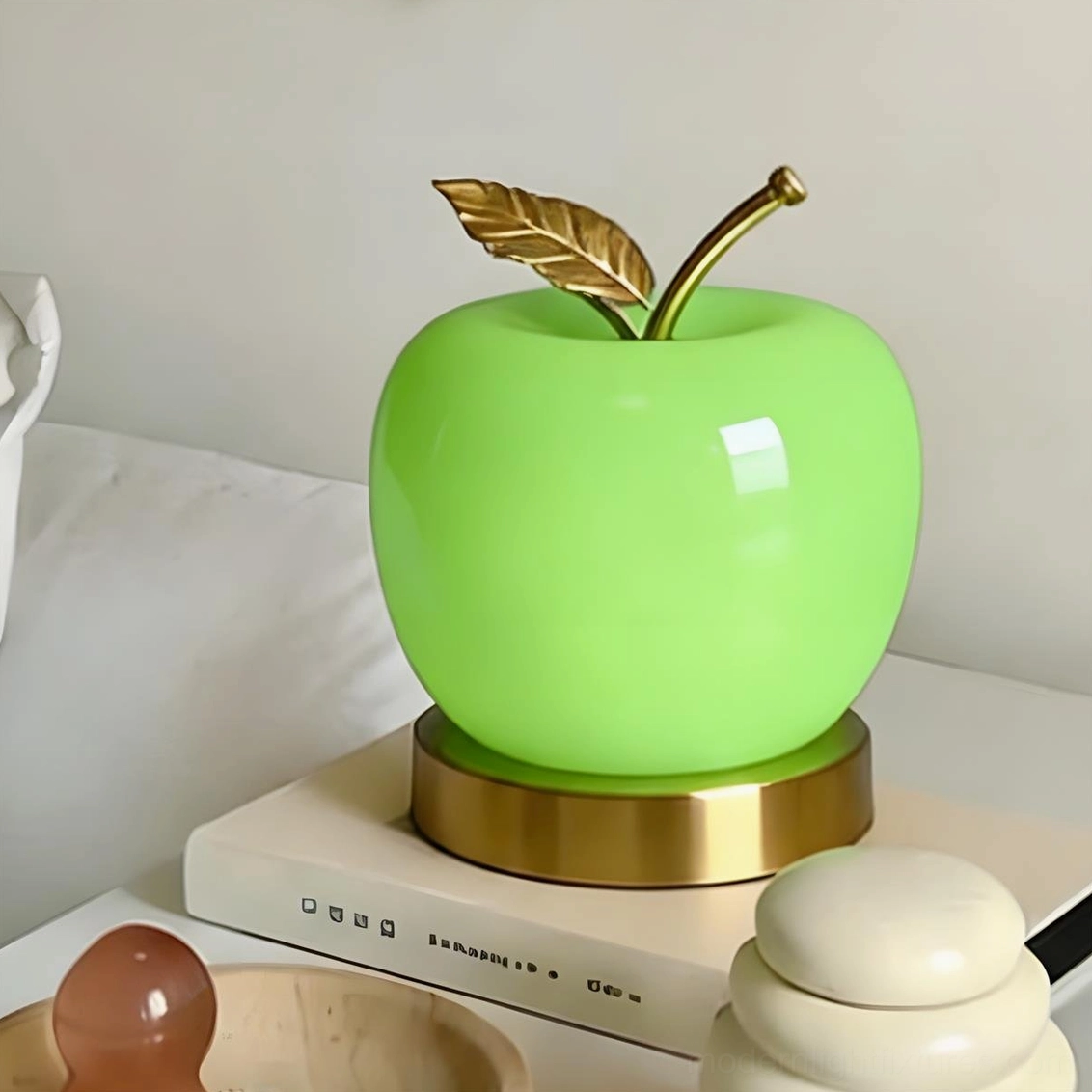 Green glossy apple shaped table lamp with gold metal accents on bedroom bedside table, three-quarter side view