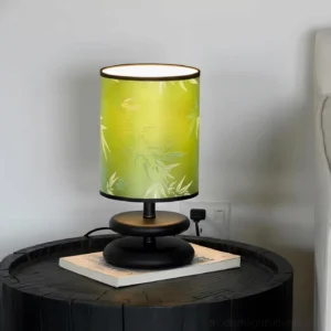 Green botanical fabric shade table lamp with black and gold base, three-quarter view on side table with stacked books