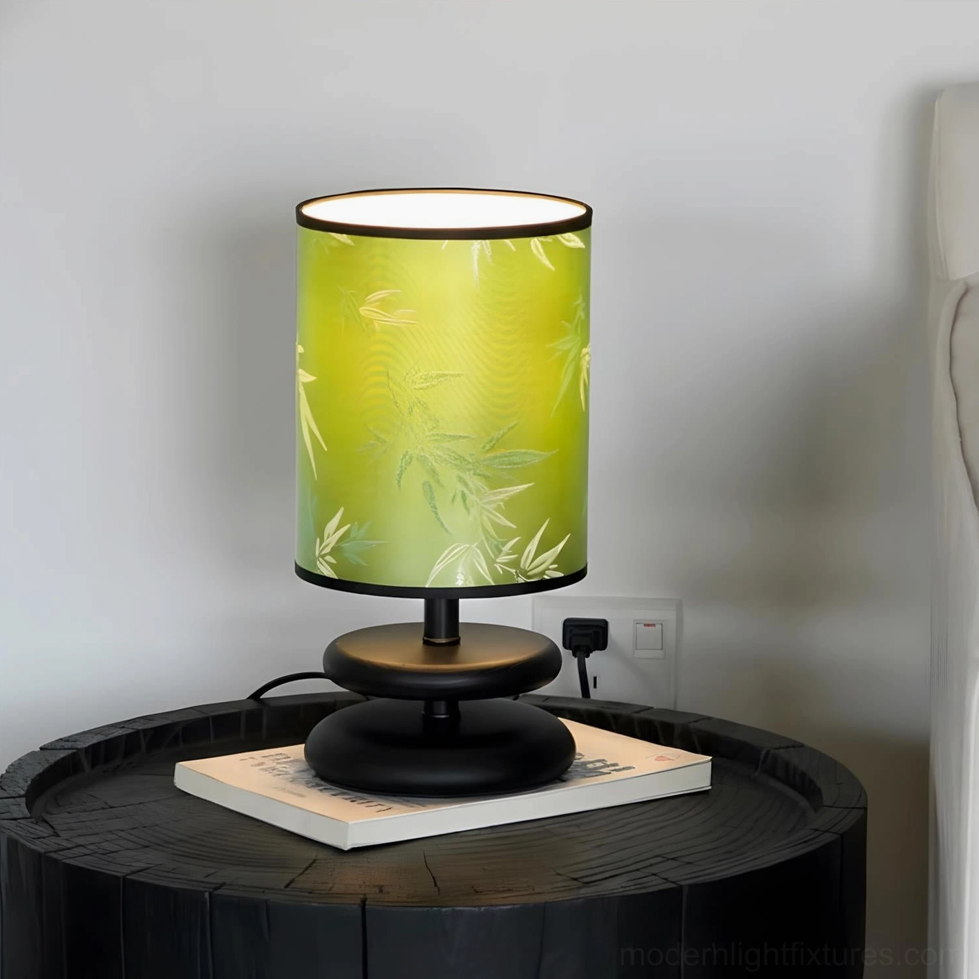 Green botanical fabric shade table lamp with black and gold base, three-quarter view on side table with stacked books