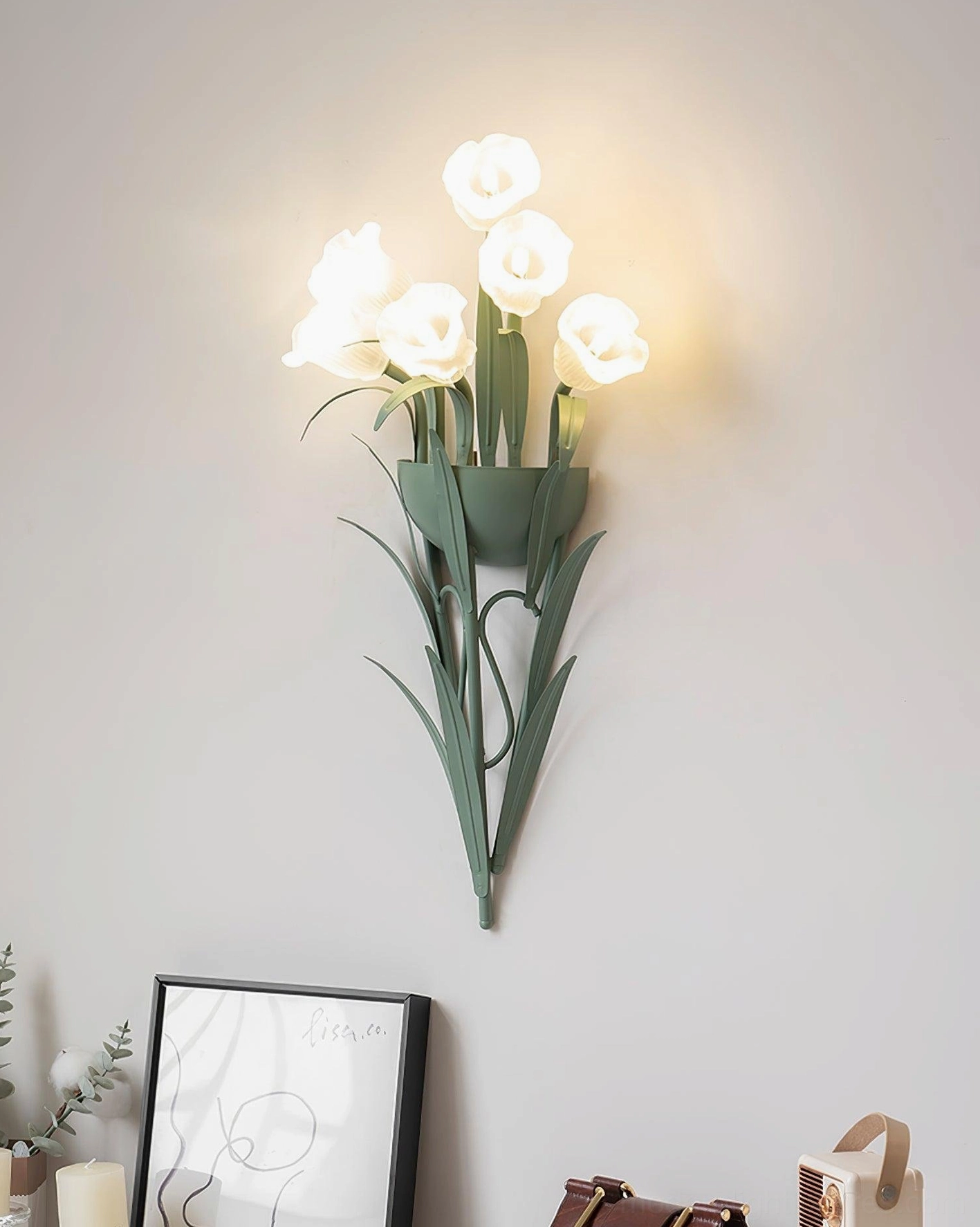 Green botanical wall sconce with lit white flowers on light gray wall, cozy Nordic pastoral light fixture
