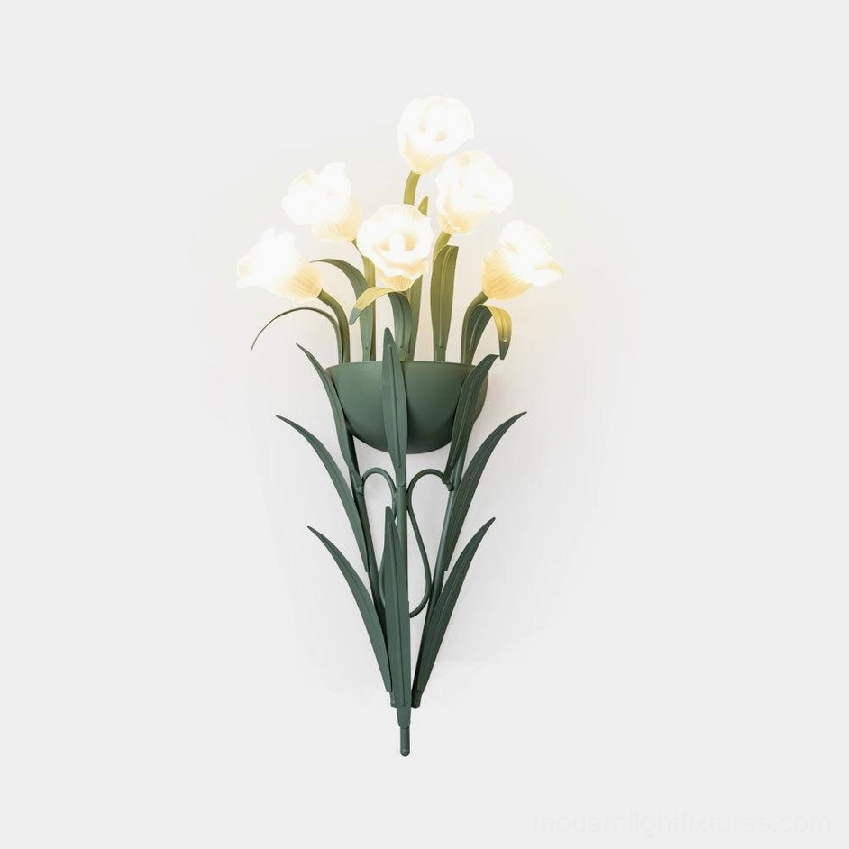 Green botanical wall sconce with white artificial flowers on plain white wall, unlit modern floral light fixture