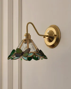 Green butterfly Tiffany-style wall lamp mounted on paneled wall, side view showing curved brass arm